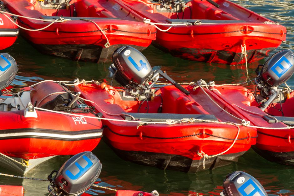 Multiple red inflatable boats with mounted outboard motors tied together on the water near a dock.