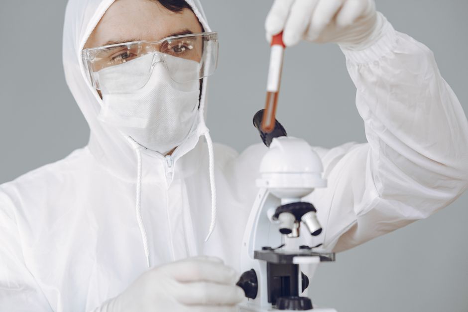 Scientist in full protective gear using a pipette with a microscope nearby in a lab setting
