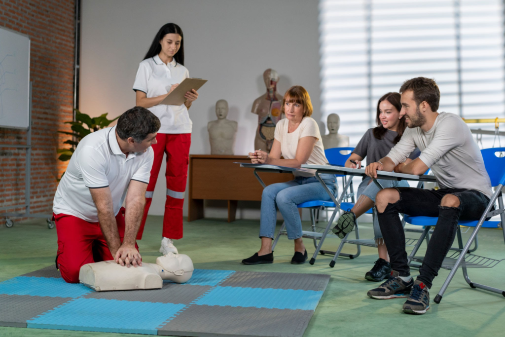 Instructor demonstrates CPR on a dummy while students watch in a classroom.